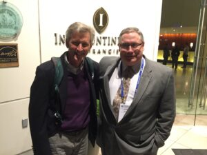 Two men dressed in suits pose for a photo at a conference.